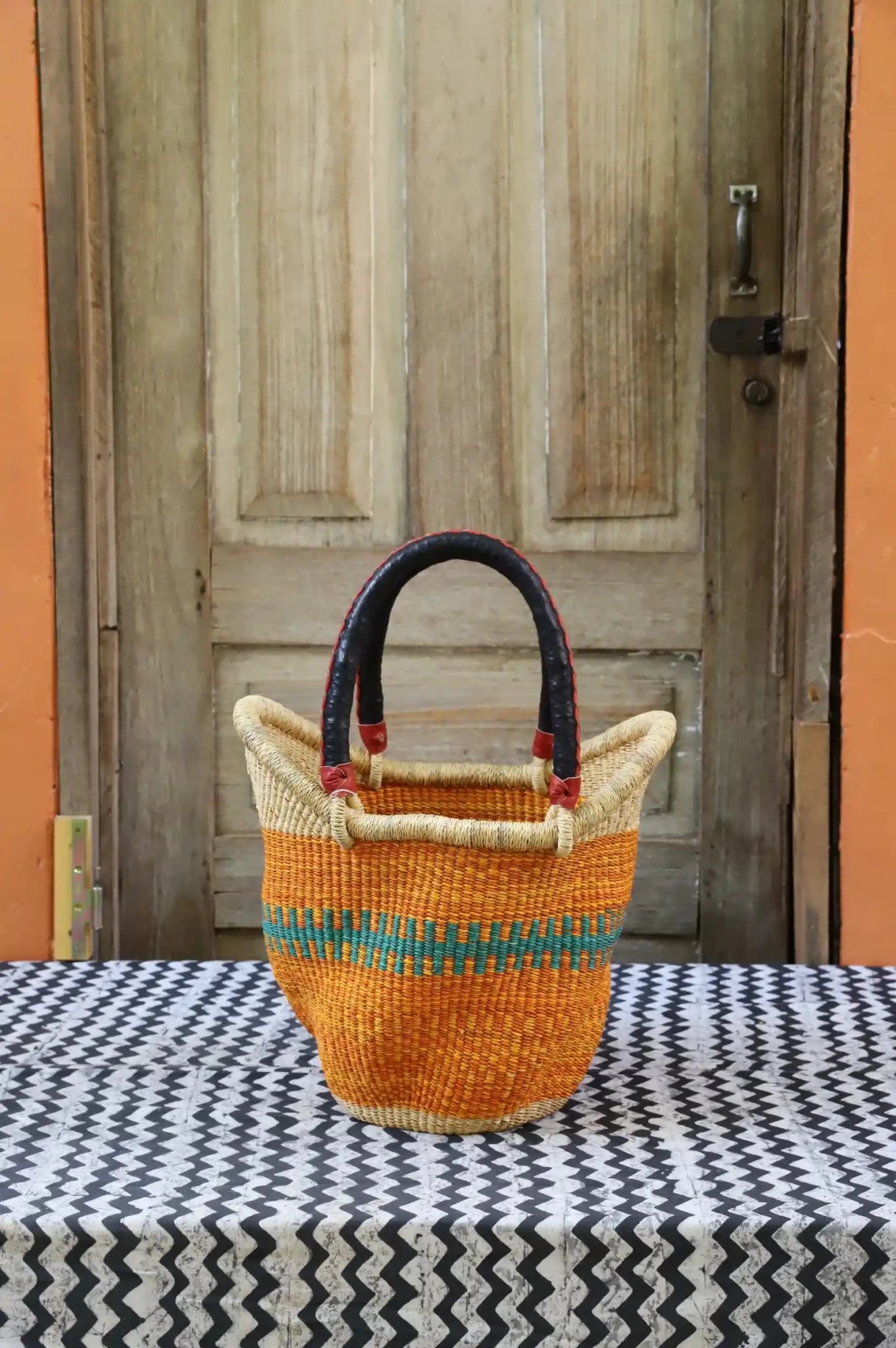 Woven carry on basket with premium leather on a black and white cloth against a wooden door