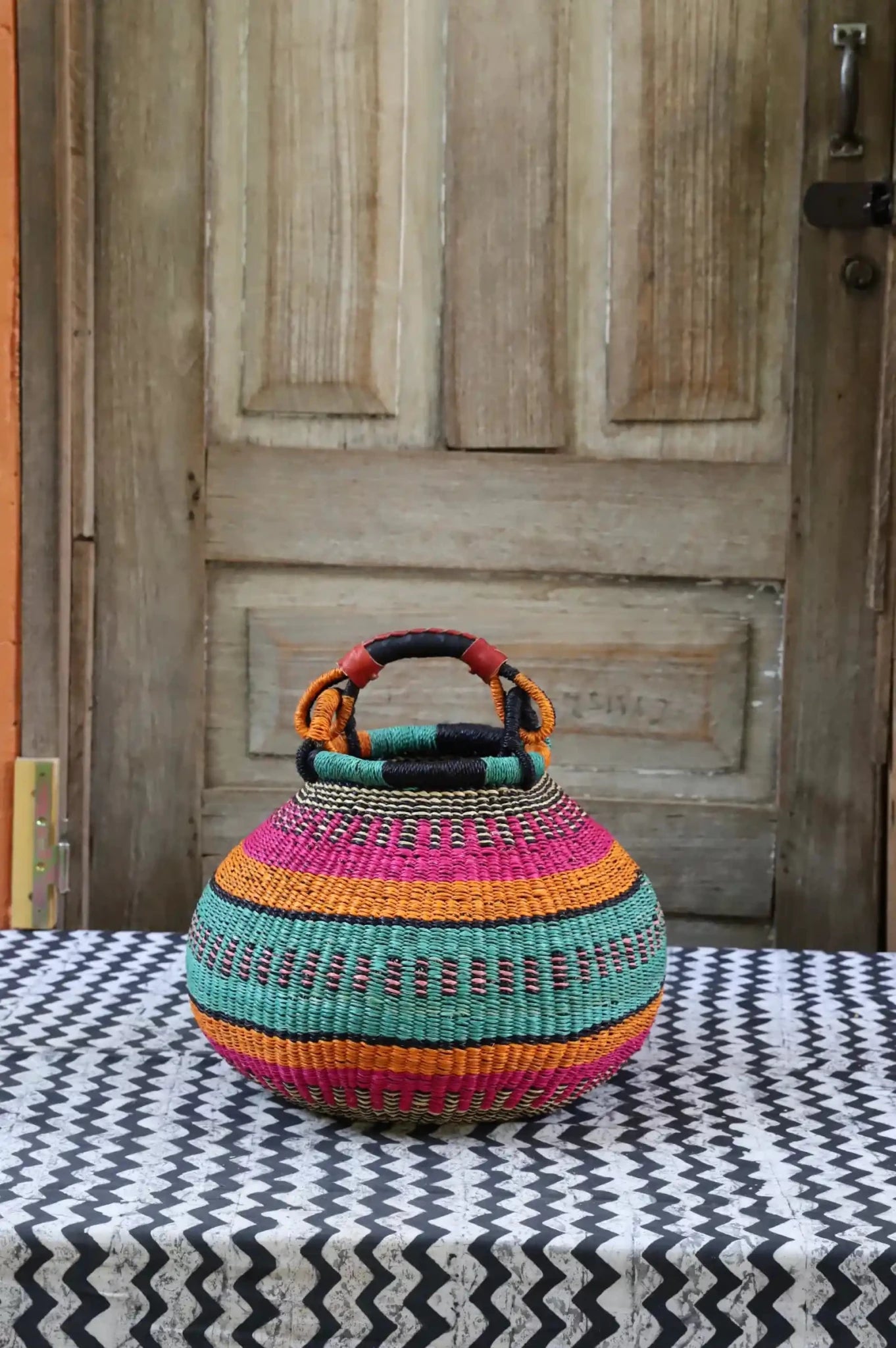 Colourful storage basket sitting on a black and white cloth against a wooden door.