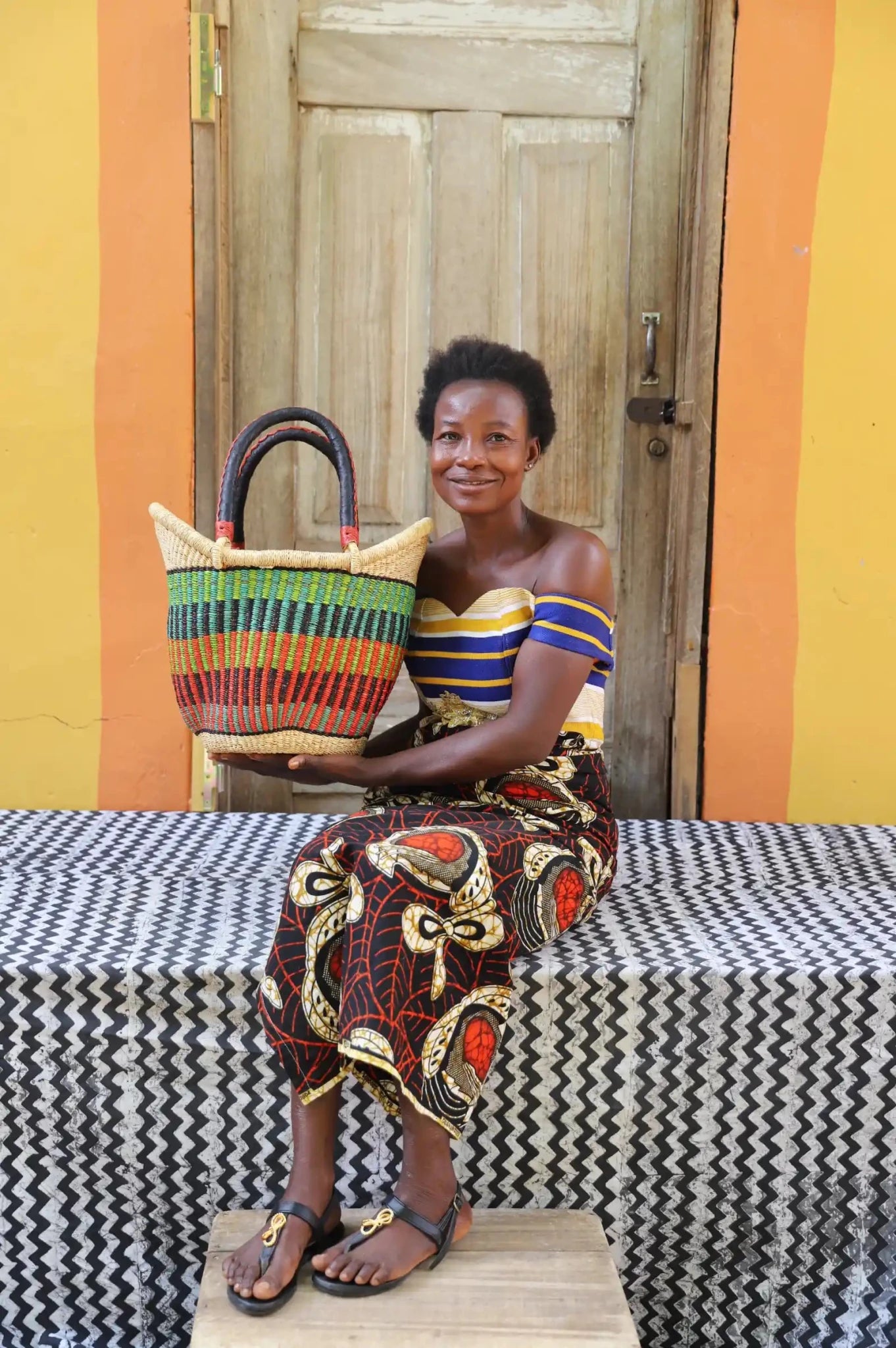 Woman in off-shoulder striped top holding a small Solara Carryall with green and multicolour stripe