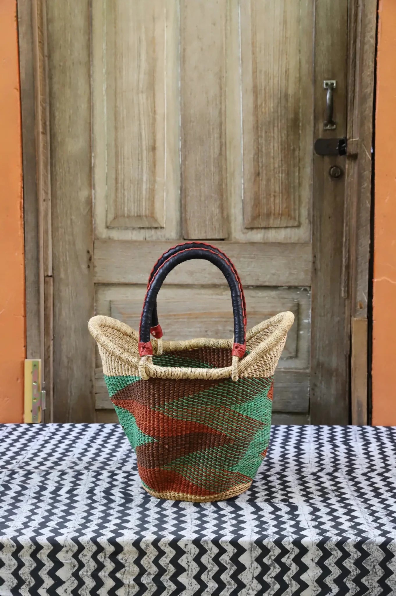 Woven carry on basket with premium leather on a black and white cloth against a wooden door