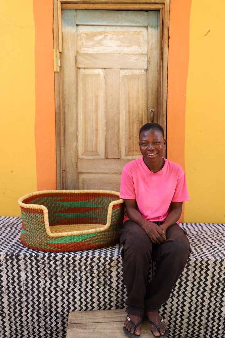 Woman sitting on a bench with a woven basket next to a wooden door and yellow wall.