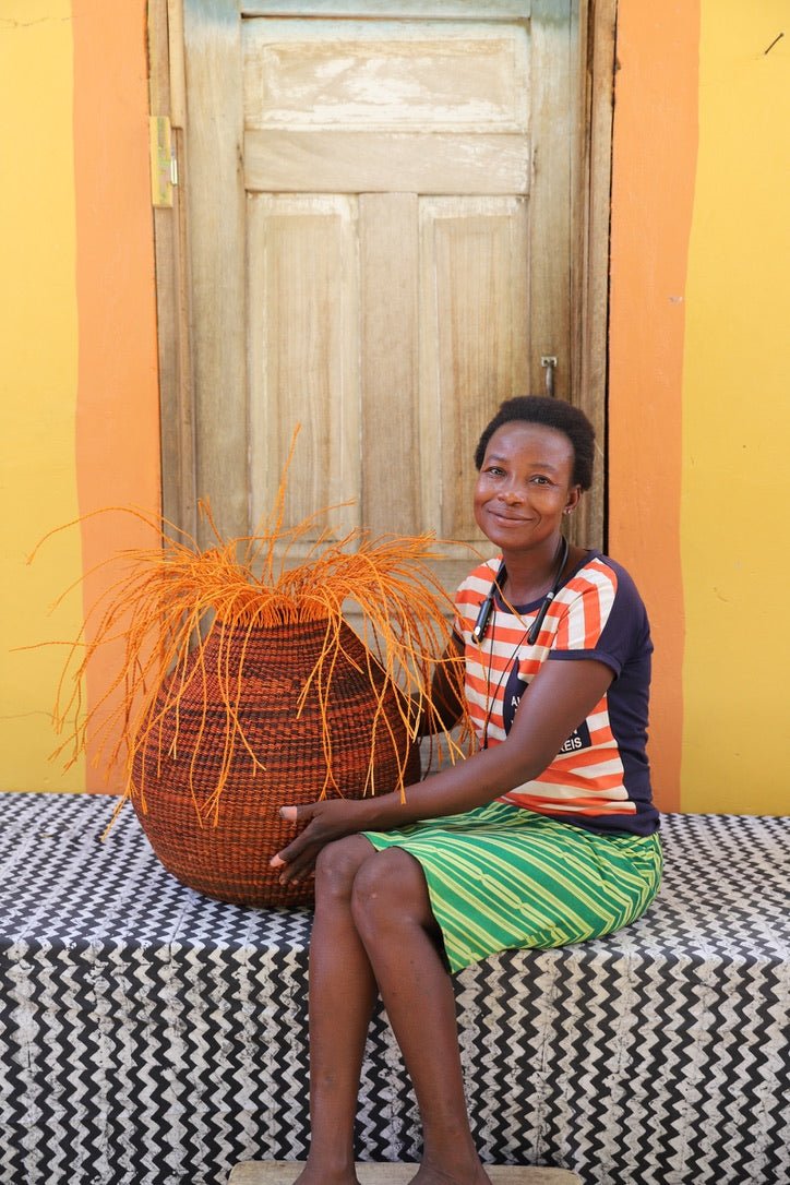 Woman sitting on a black and white cloth with a woven basket against a colorful wall.