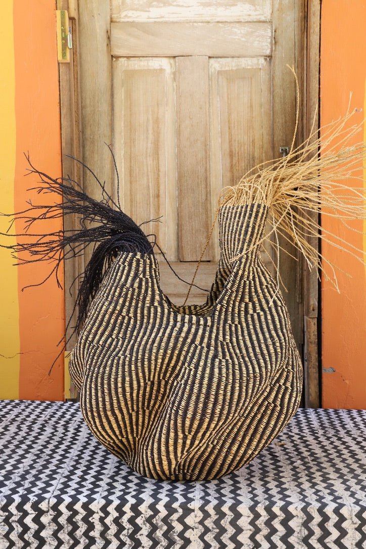 A handwoven piece sitting on a black and white cloth with decorative straw branching out against a wooden door