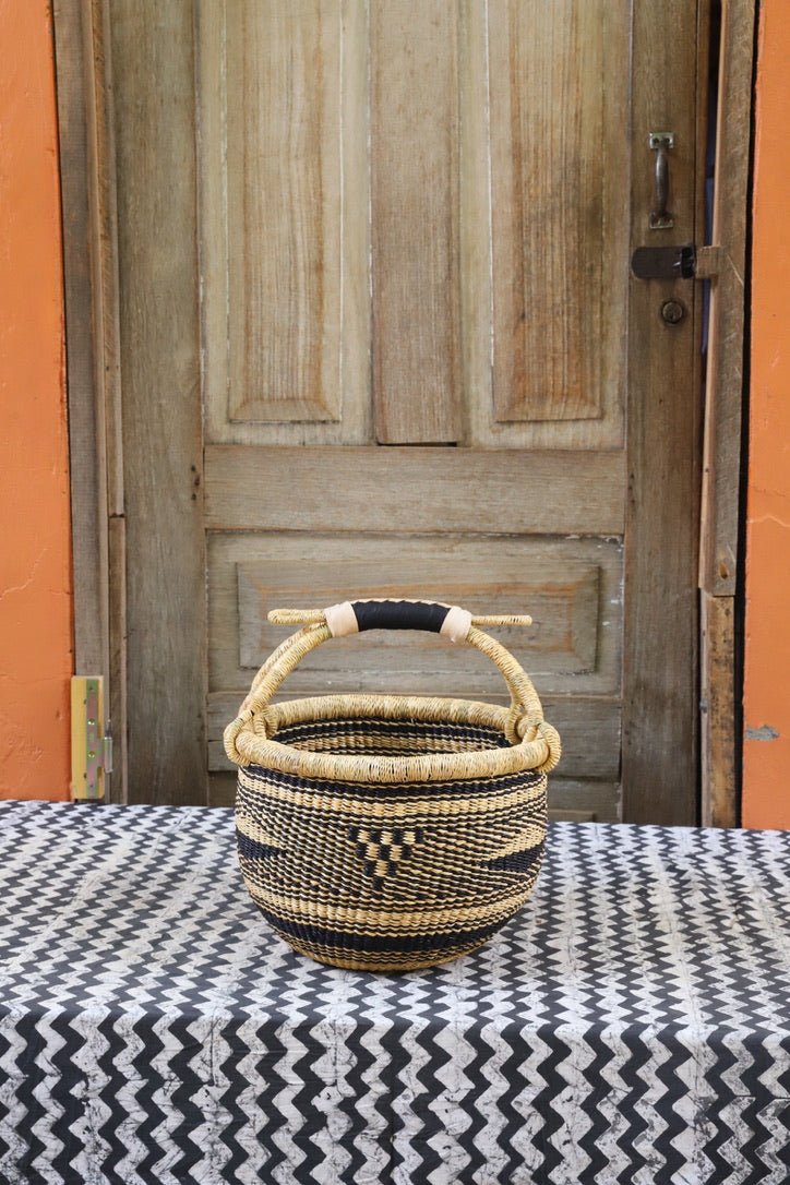 Woven carry on bag with premium leather handles on a black and white cloth against a wooden door.