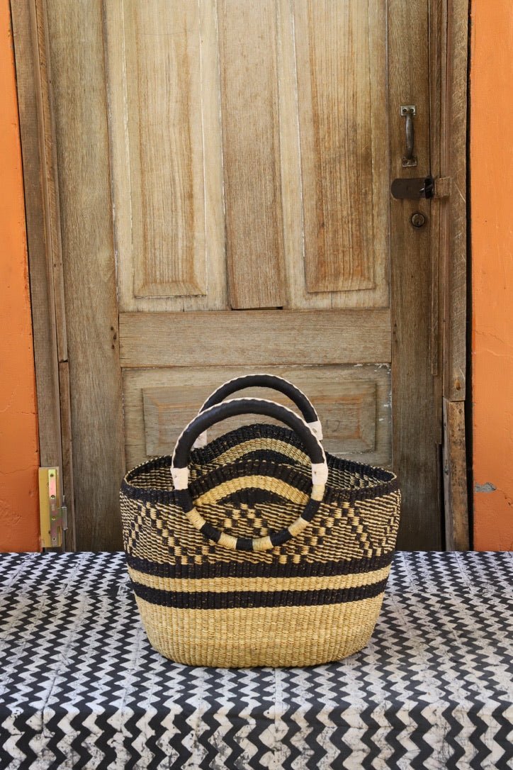 Woven carry on basket with premium leather on a black and white cloth against a wooden door