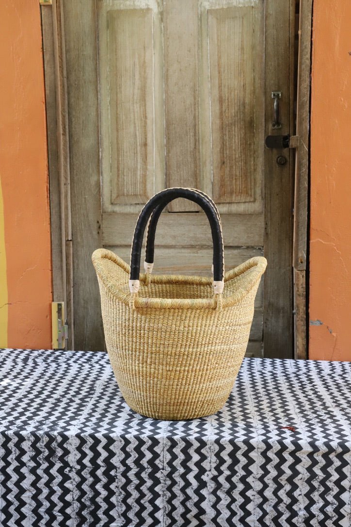 Woven basket with black handles on a tablecloth in front of a wooden door.
