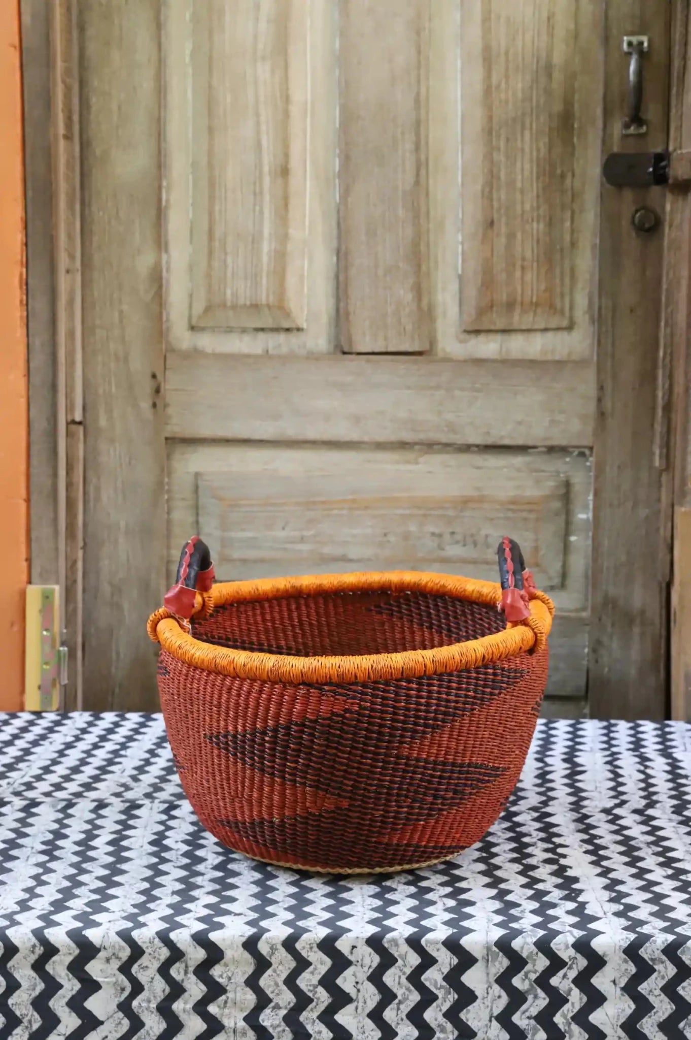 A colorful handwoven storage basket sitting on a black and white cloth against a wooden door