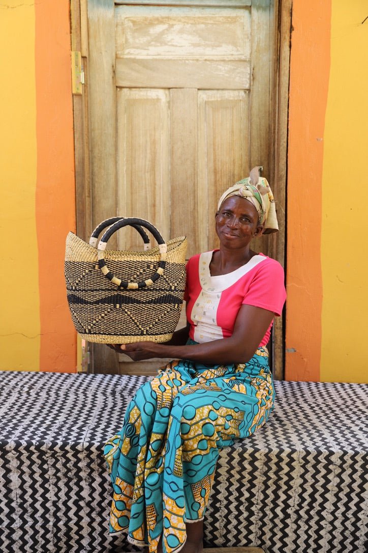 Woman holding a woven bag in front of a colorful wall.