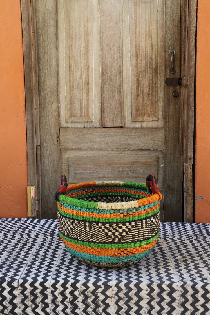 A colorful handwoven storage basket sitting on a black and white cloth against a wooden door