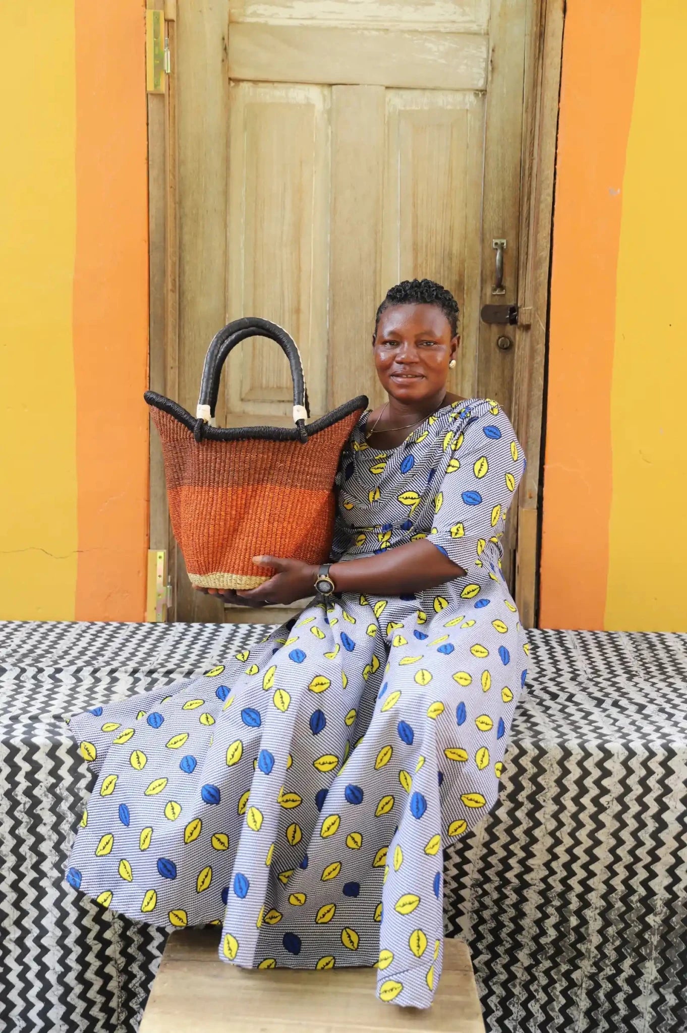 Woman in blue leaf-print dress holding a small Solara Carryall with solid rust body, dark leather handles