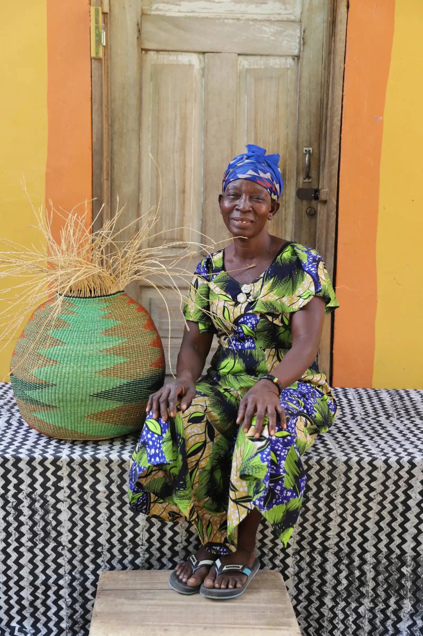Woman in traditional attire sitting on a bench with a colorful woven basket .