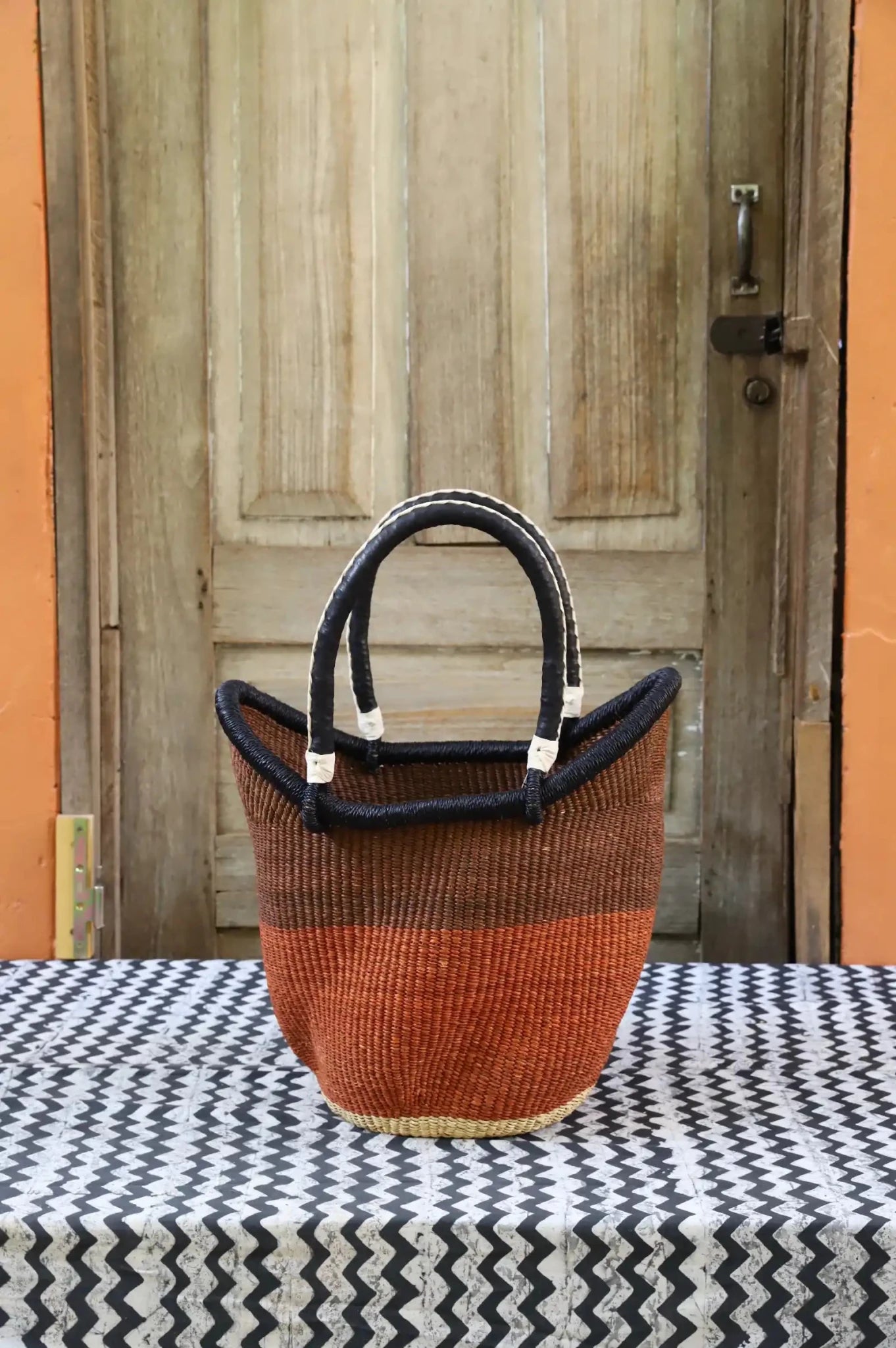 Woven carry on basket with premium leather on a black and white cloth against a wooden door