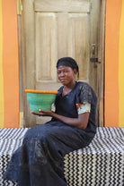Woman holding a green basket in front of a wooden door with an orange wall.