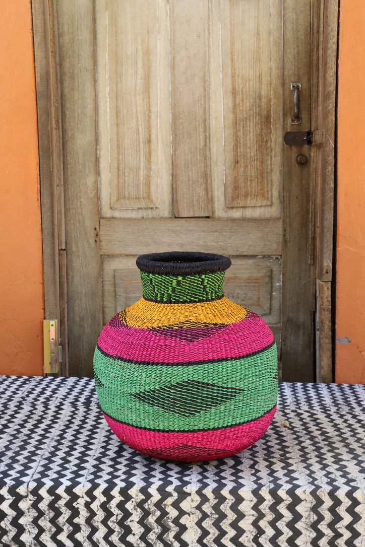 Decorative handwoven basket with colorful patterns on a black and white cloth against a wooden door.