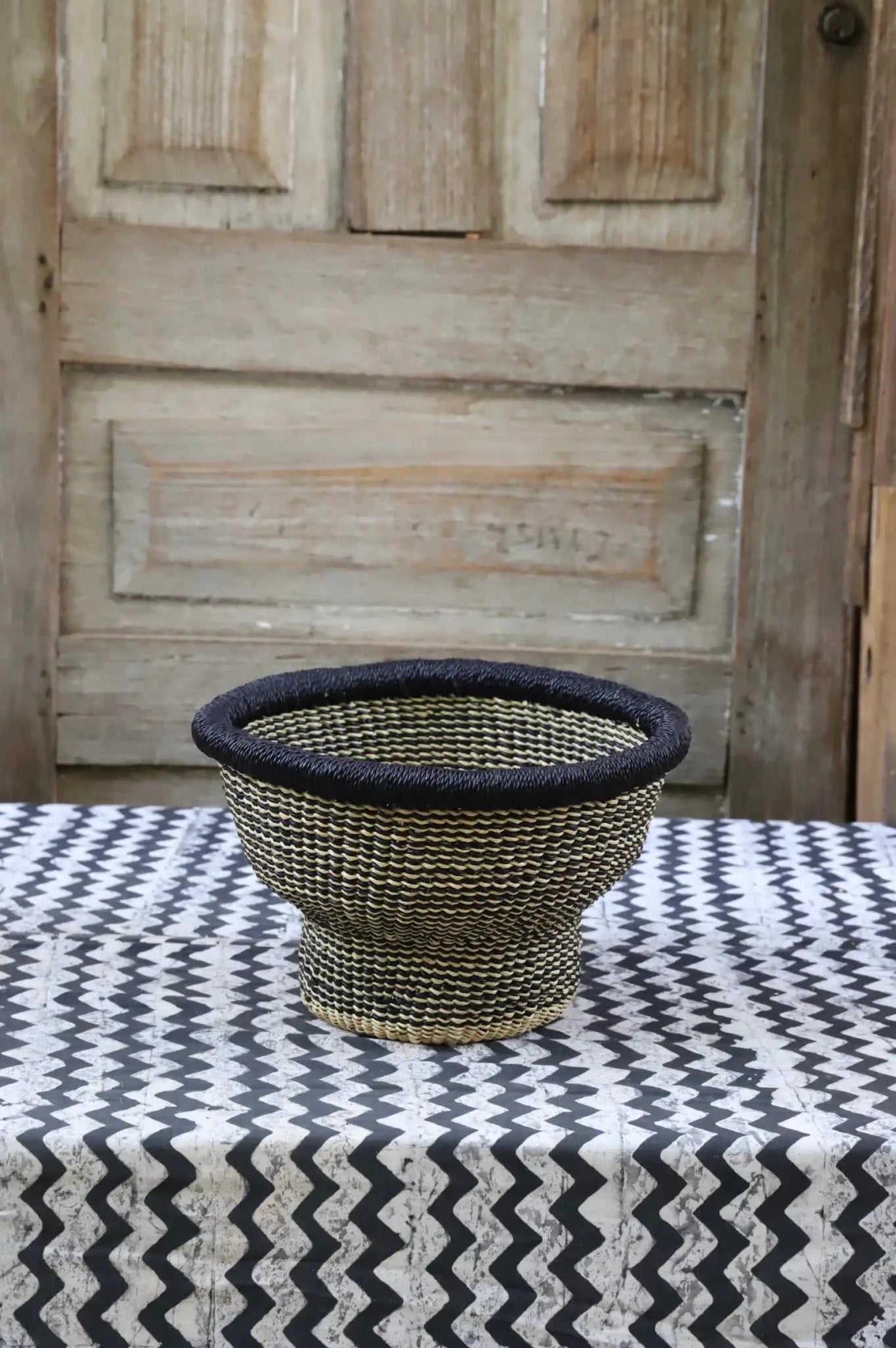 Woven storage basket with a beautiful pattern on a black and white cloth against a wooden door.