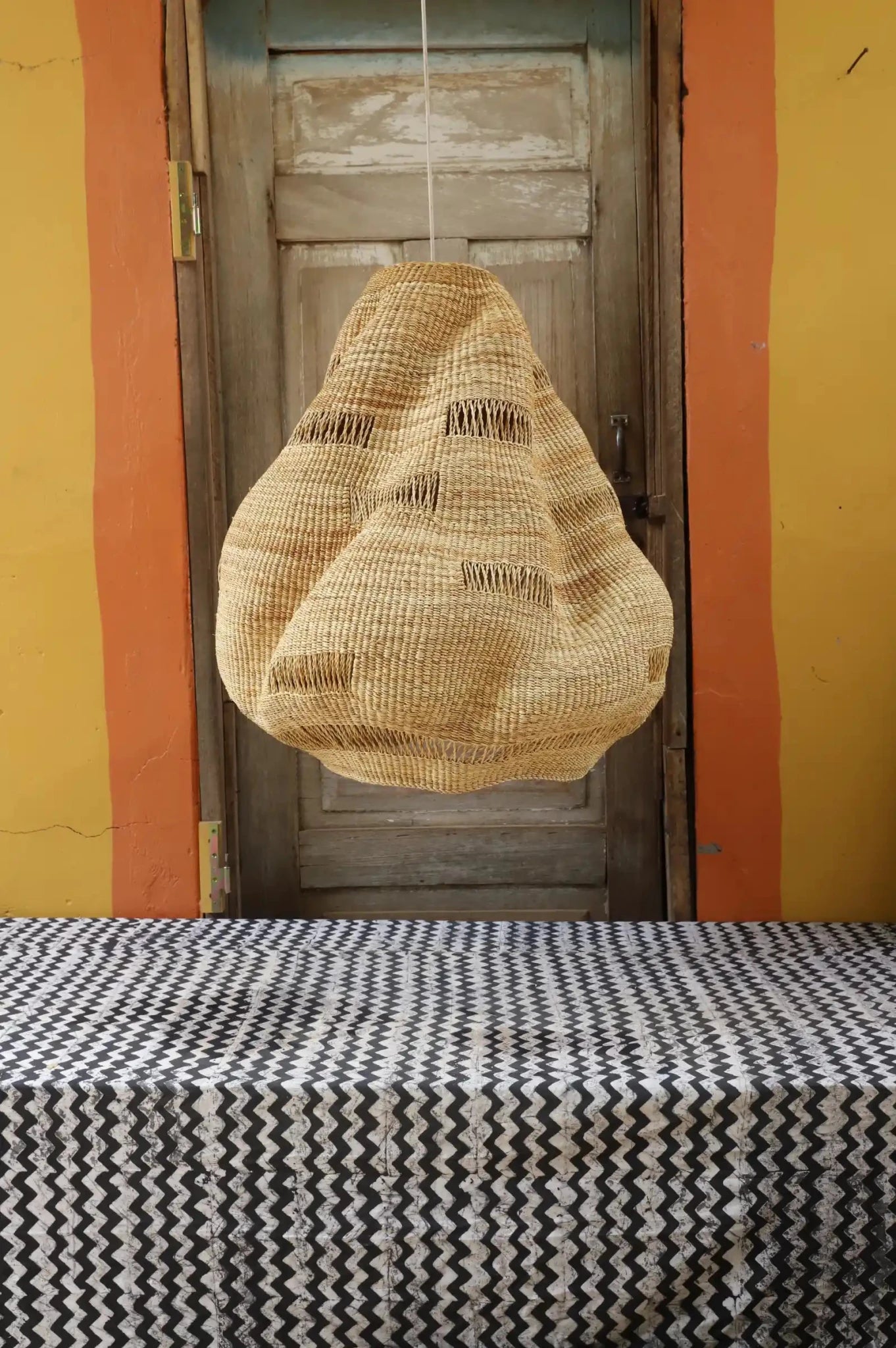 Woven basket hanging above a table with a striped tablecloth against a yellow wall.