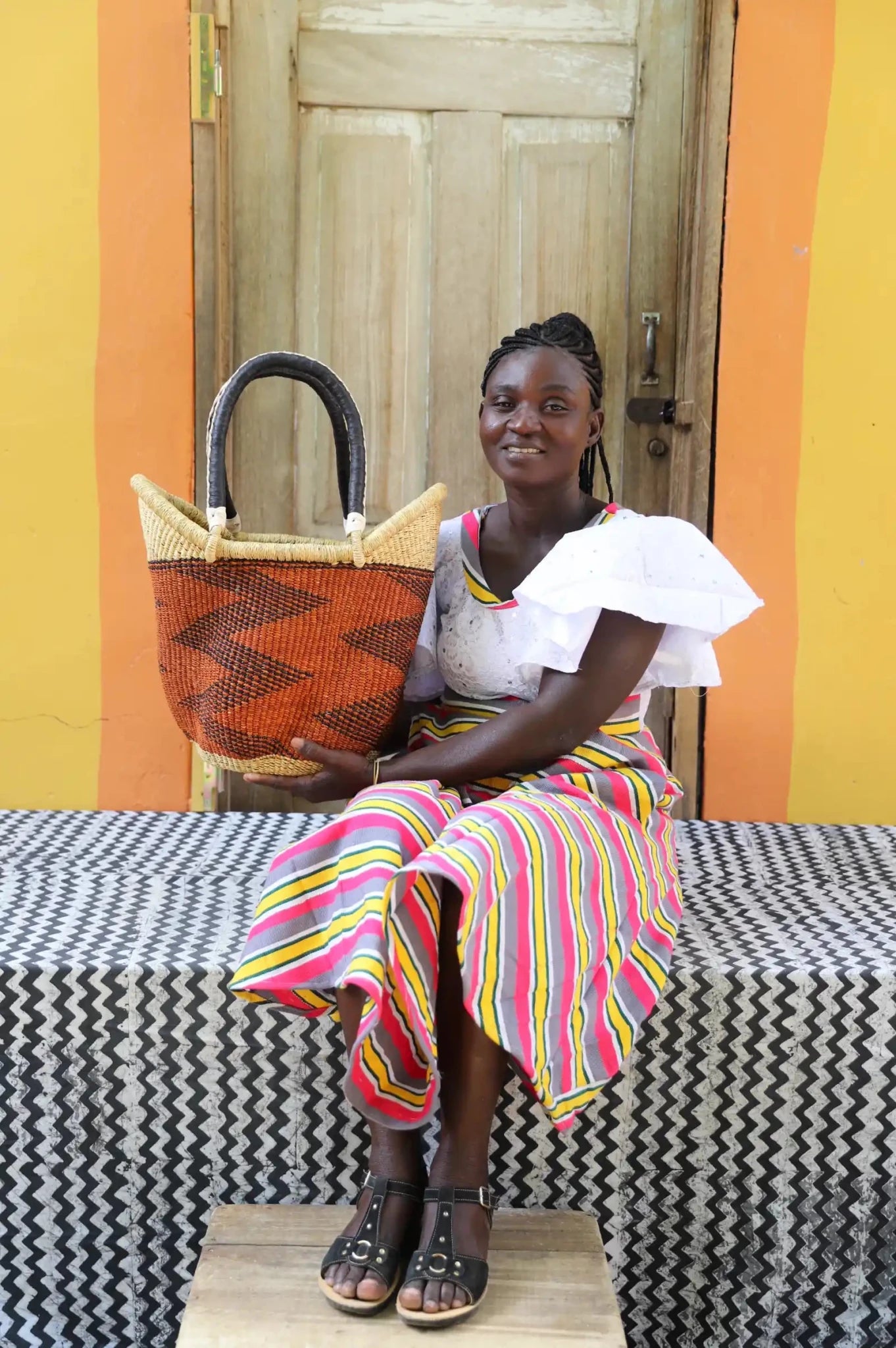 Woman in white ruffled top seated holding a medium rust Solara Carryall with dark zigzag pattern