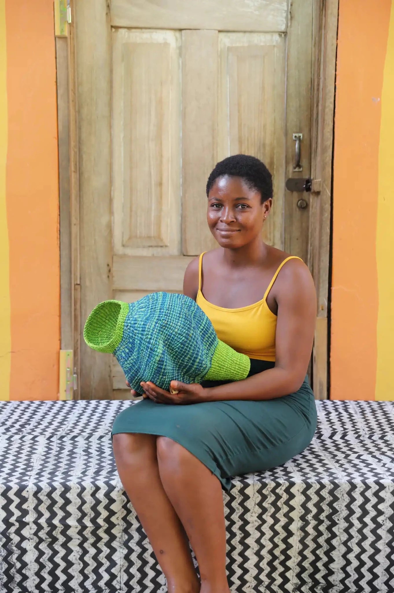 Woman holding a woven conch piece on a black and white patterned surface with a wooden door in the background.