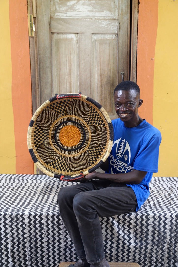 Man holding a woven basket in front of a wooden door with a yellow wall.