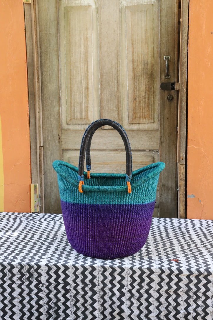 Woven handbag with teal top and purple bottom on a table with a wooden door in the background.