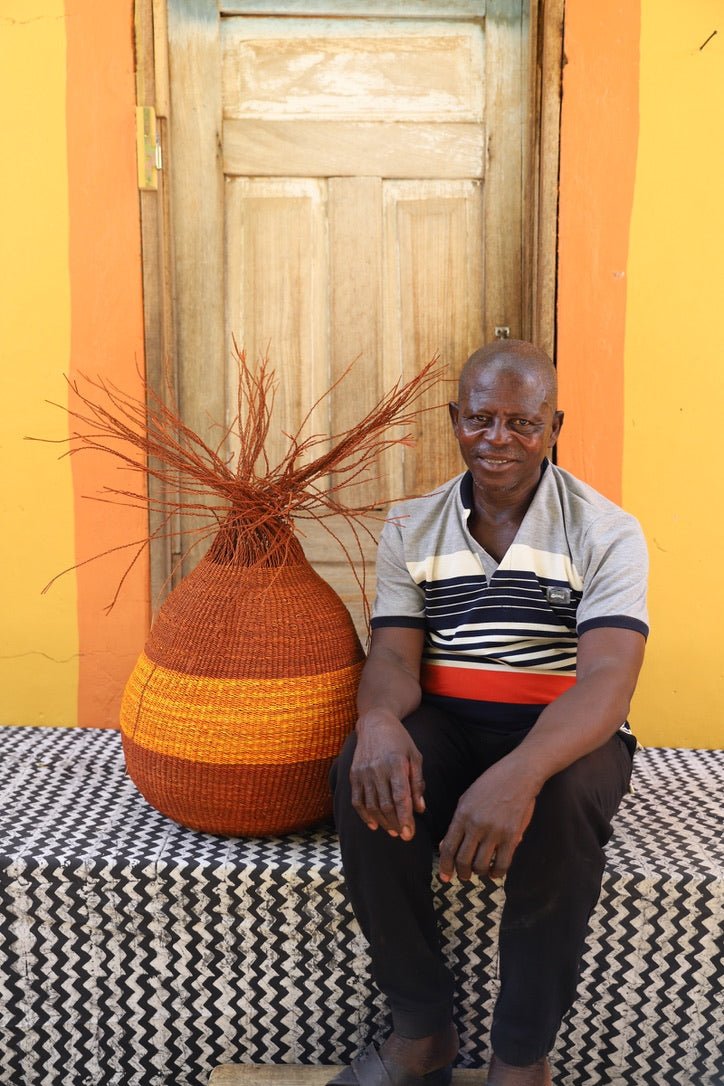 Man sitting with a colorful woven décor basket on a black and white cloth with a wooden door in the background.