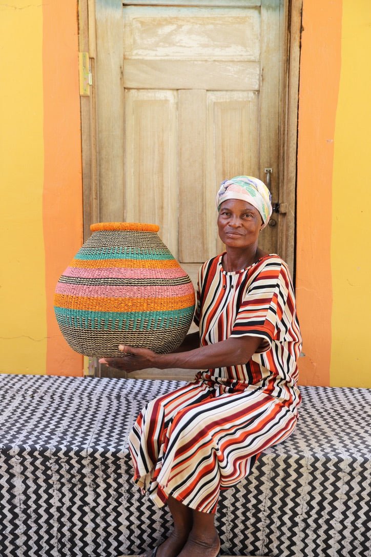 Woman holding a colorful woven vase against a vibrant yellow wall.