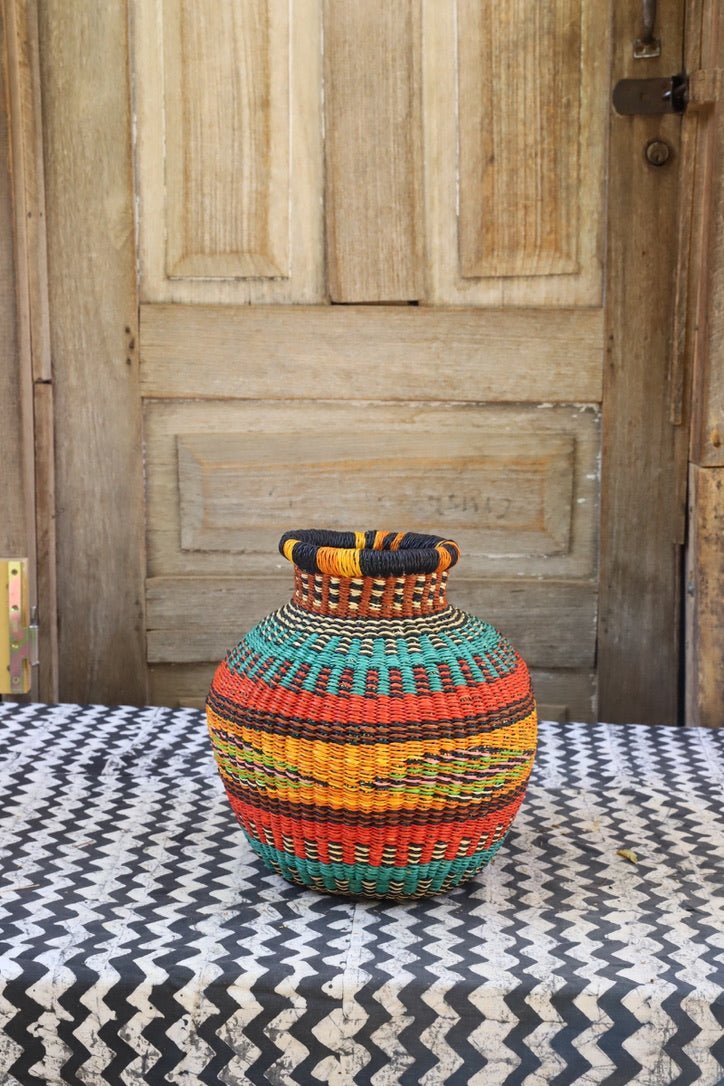 Decorative handwoven basket with colorful patterns on a black and white cloth against a wooden door.