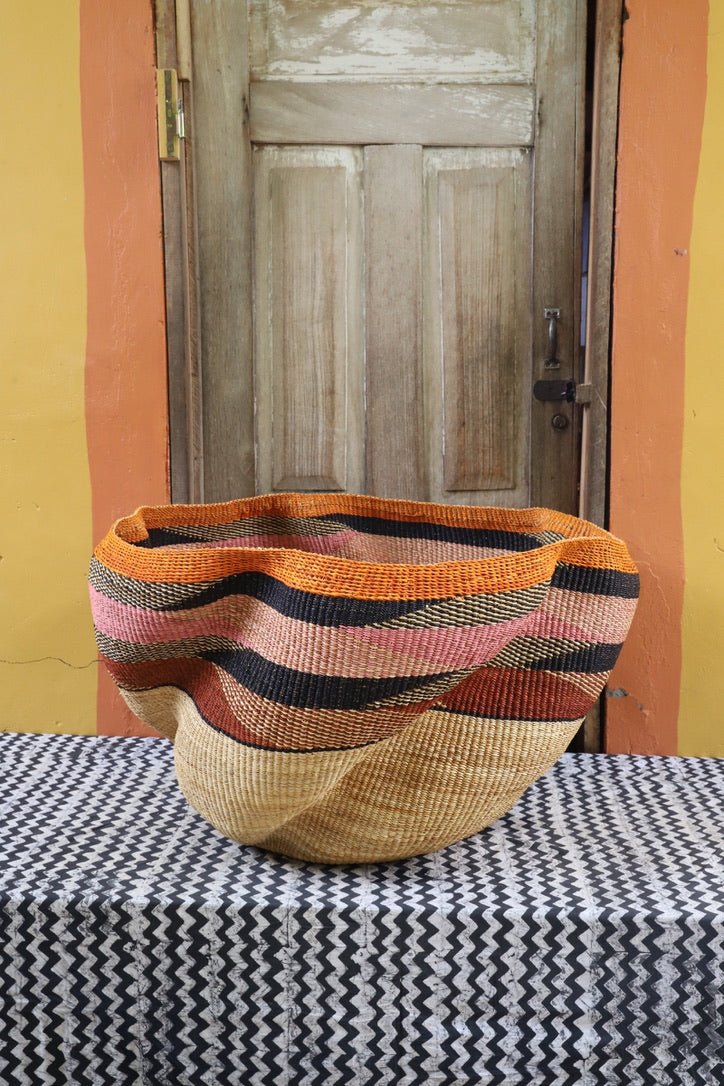 Large woven basket with geometric pattern on a black and white checkered tablecloth in front of a wooden door.
