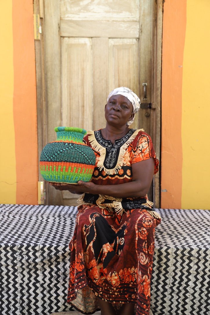 Woman holding a colorful woven basket in front of a wooden door with an orange wall.