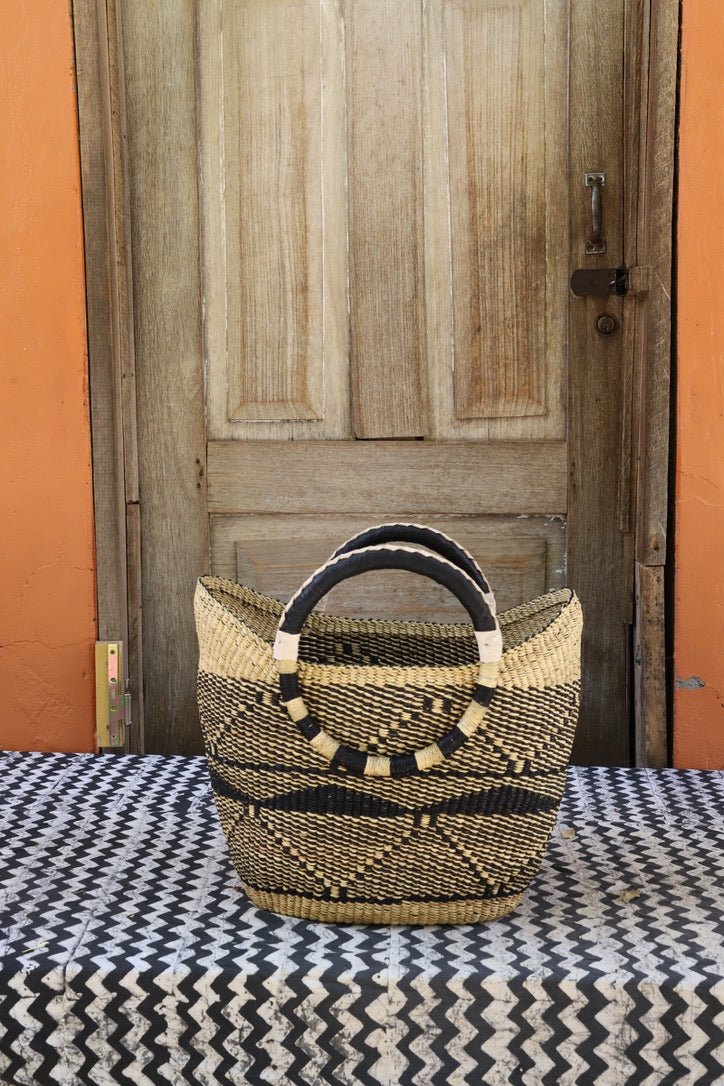 Woven carry on basket with premium leather on a black and white cloth against a wooden door