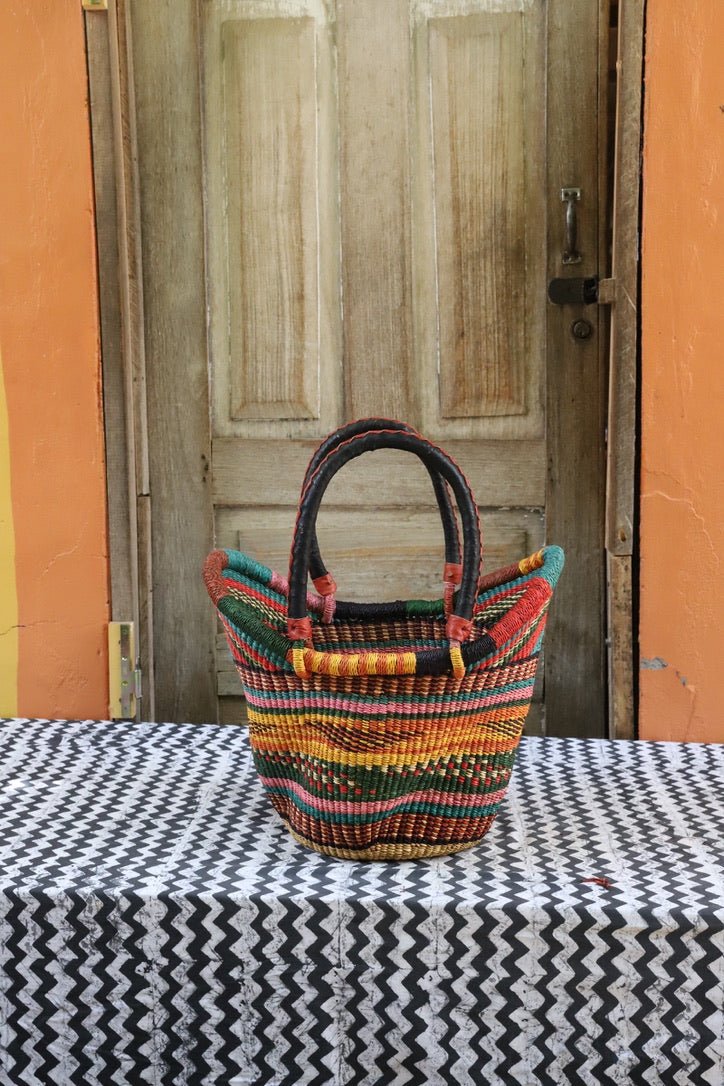 Woven basket with colorful patterns on a tablecloth in front of a wooden door.
