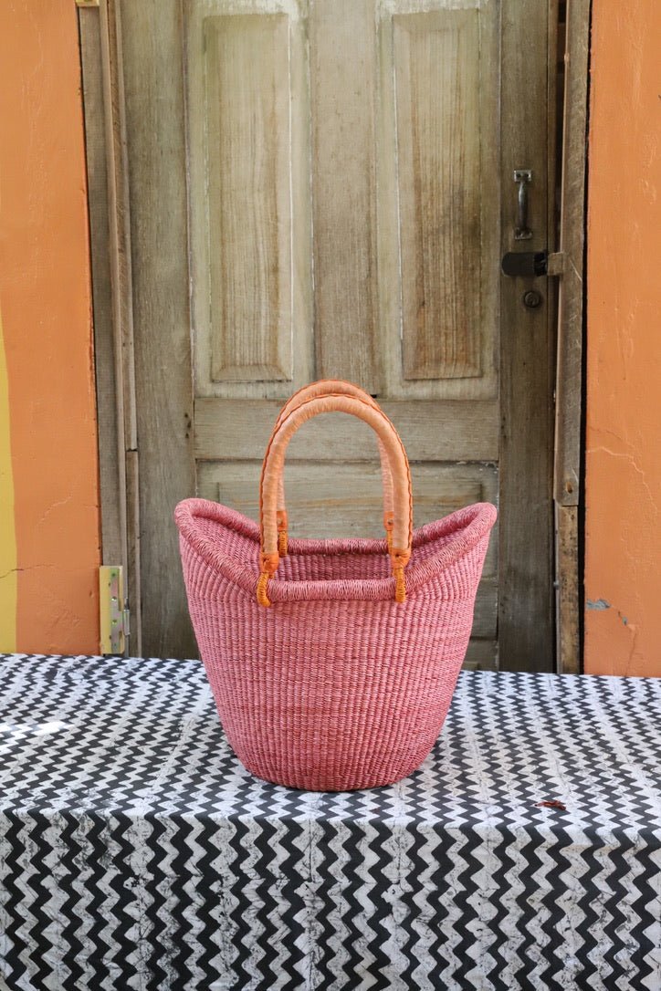 Pink woven basket with wooden handles on a black and white patterned tablecloth in front of a wooden door.