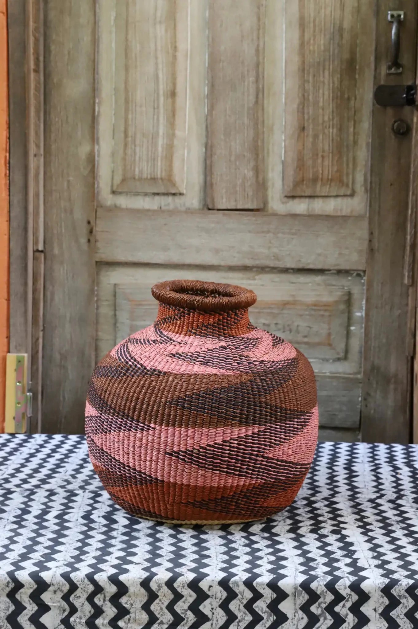 Decorative handwoven basket with colorful patterns on a black and white cloth against a wooden door.