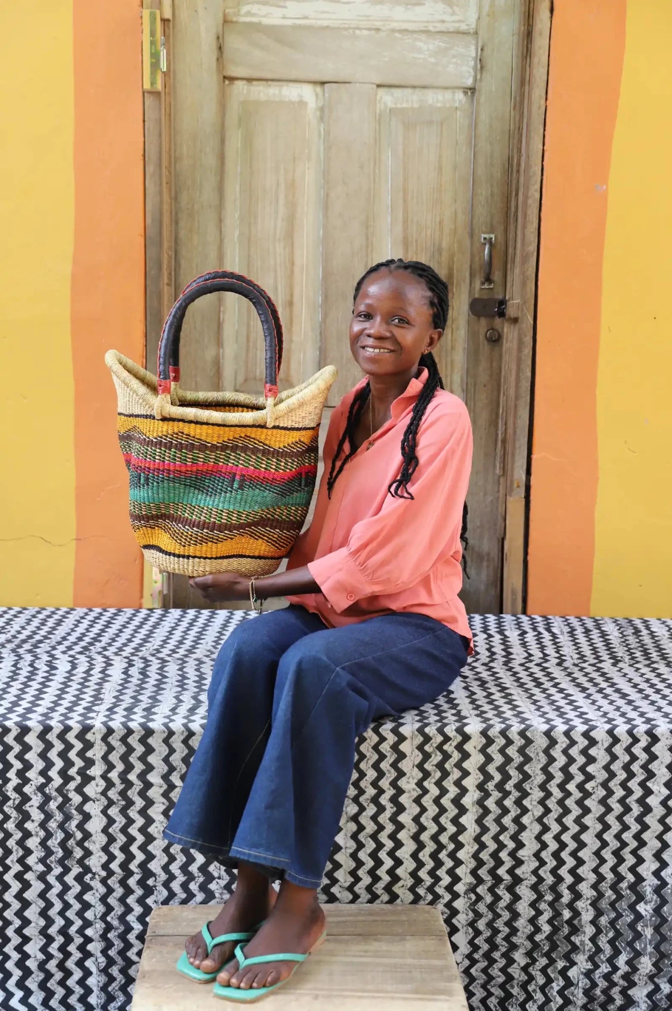 Woman in peach shirt holding a medium golden Solara Carryall with multicolour stripe band, leather handles