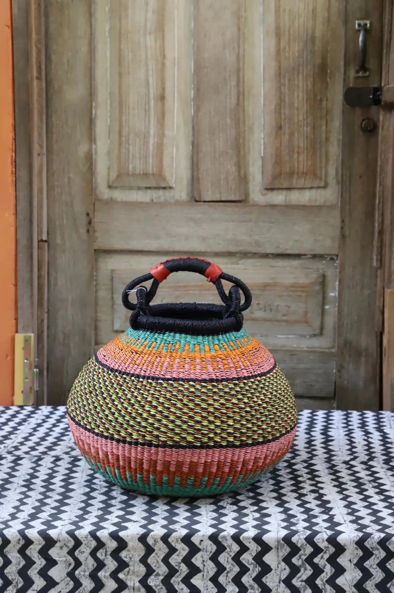 Colourful storage basket sitting on a black and white cloth against a wooden door.