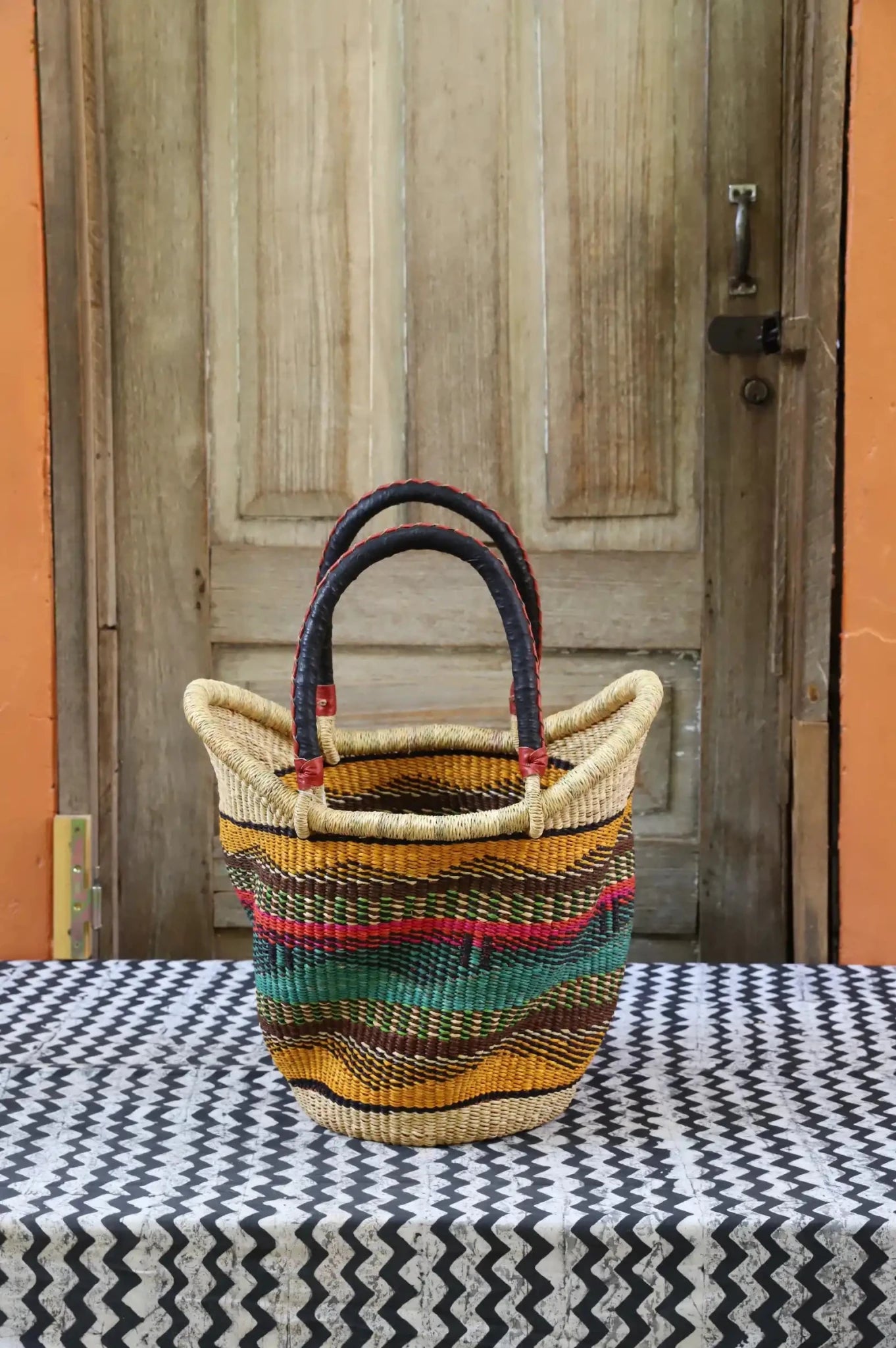 Woven carry on basket with premium leather on a black and white cloth against a wooden door