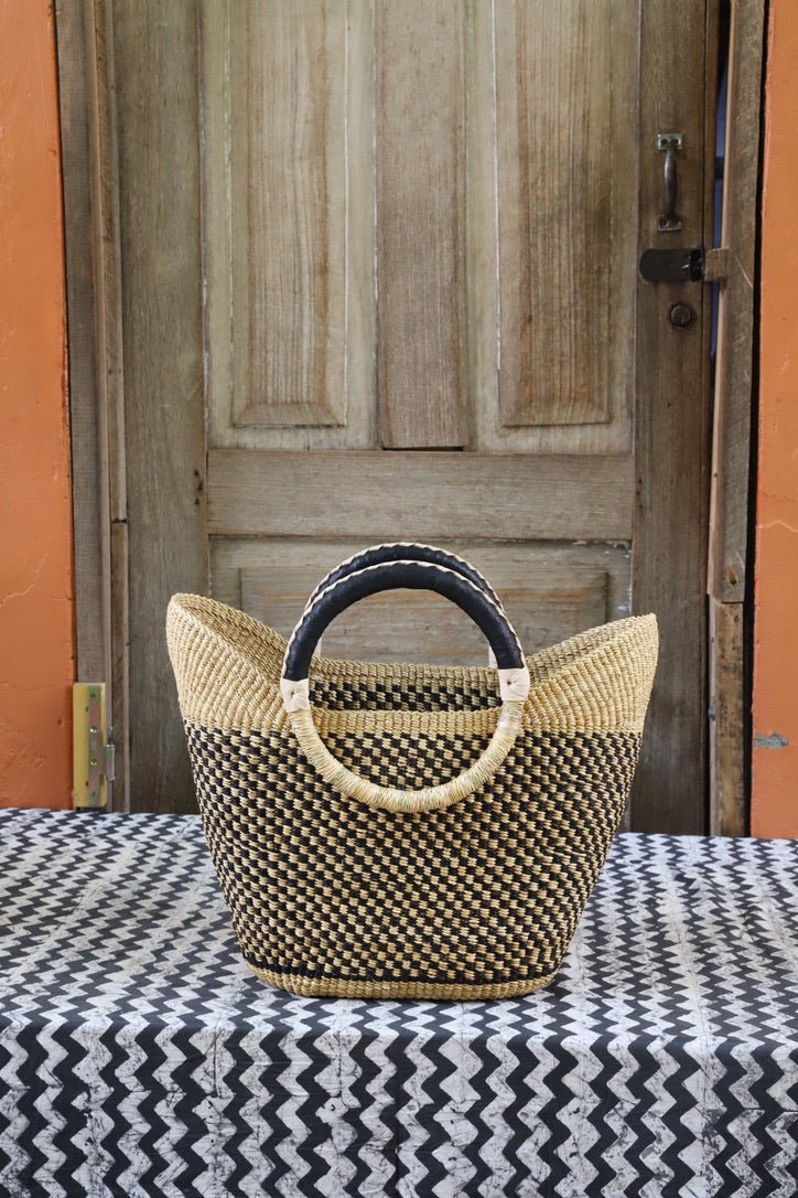 Woven carry on basket with premium leather on a black and white cloth against a wooden door
