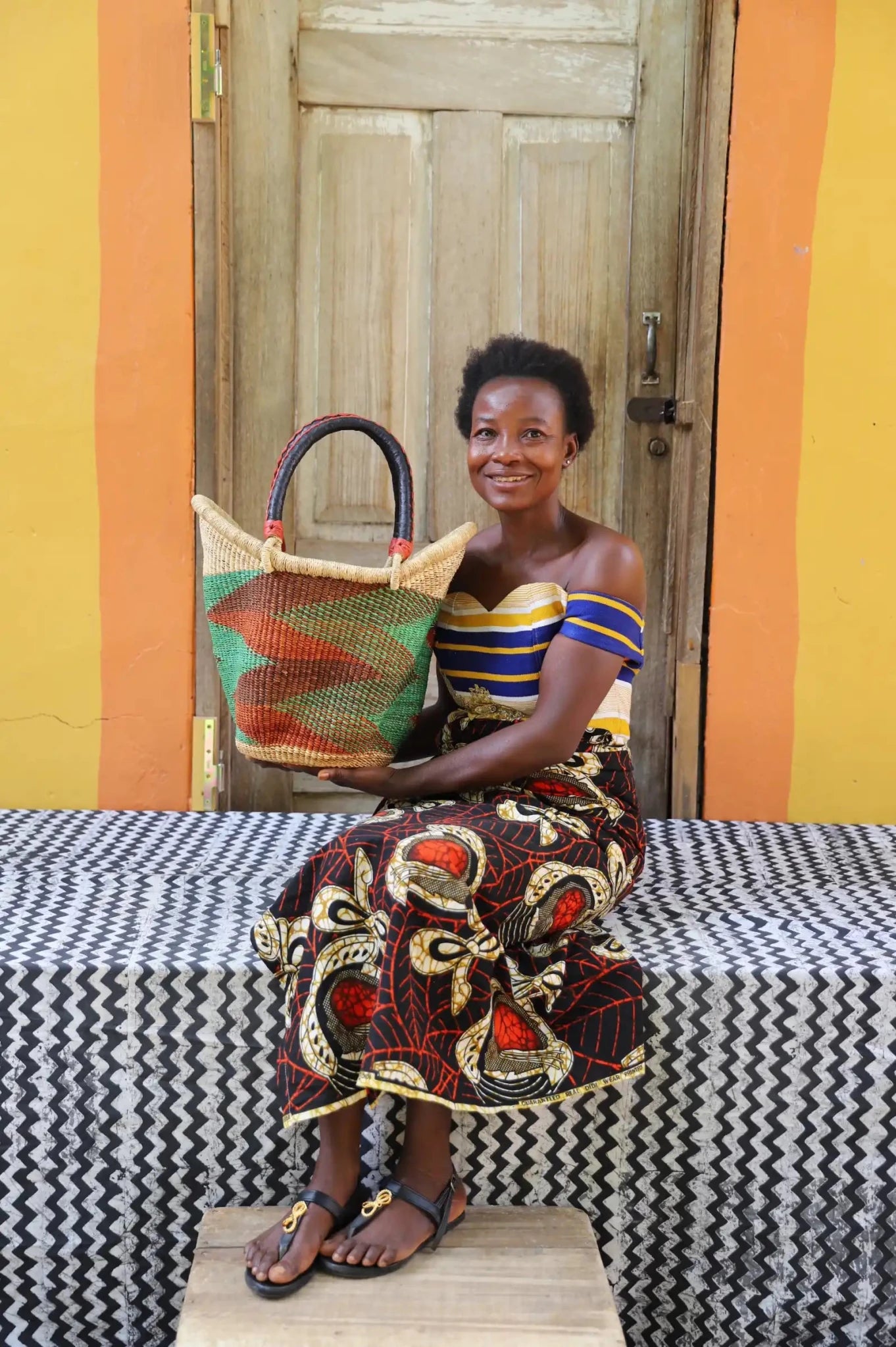 Woman in striped off-shoulder top holding a small green camouflage-patterned Solara Carryall