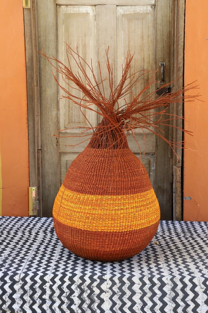 Colorful woven décor basket with straw branching out on a black and white cloth with a wooden door in the background.
