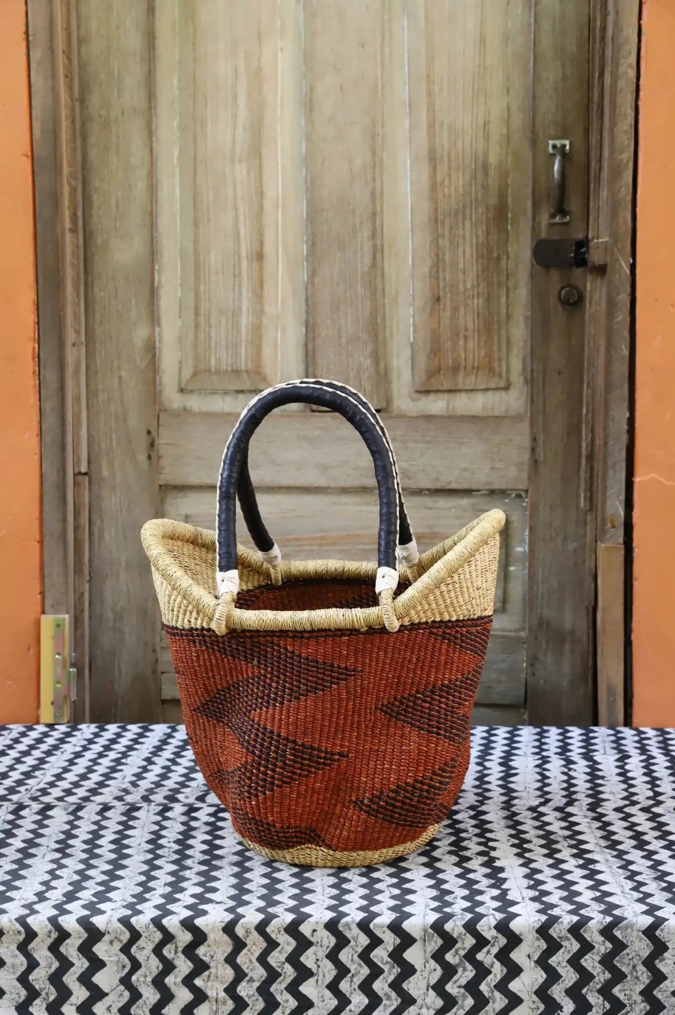 Woven carry on basket with premium leather on a black and white cloth against a wooden door