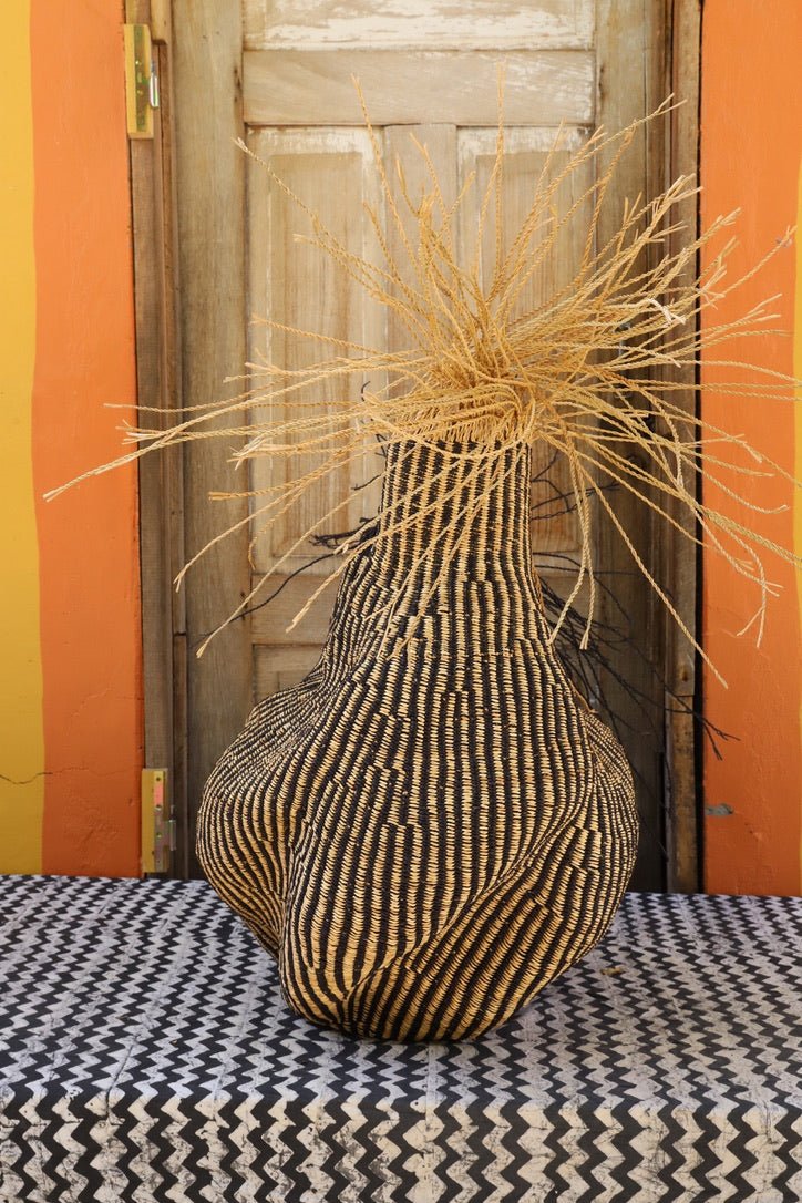 Decorative basket with stylish straw branching out on a black and white cloth against a wooden door.