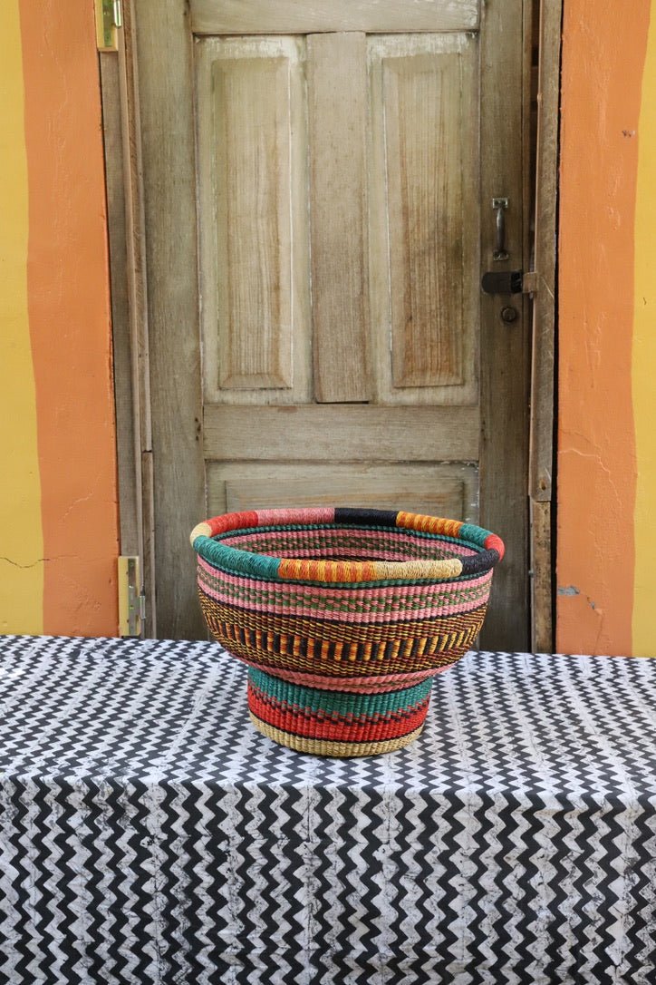 Colorful woven basket on a black and white patterned tablecloth with a wooden door in the background.