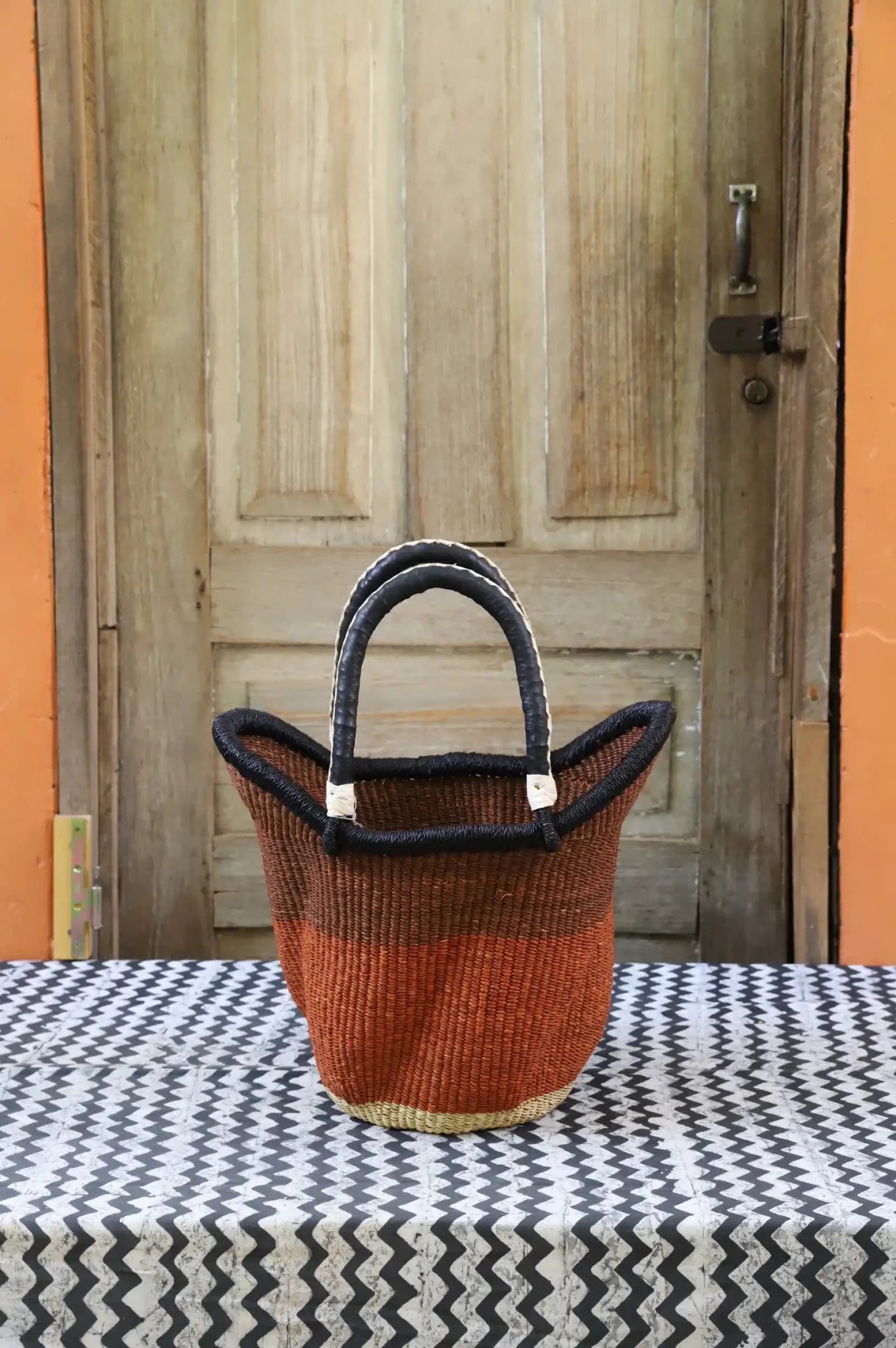 Woven carry on basket with premium leather on a black and white cloth against a wooden door