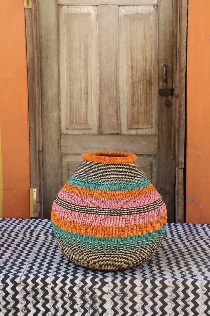 Colorful woven décor basket on a black and white cloth with a wooden door in the background.