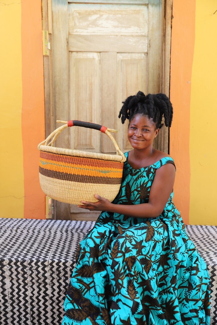 Woman with dreadlocks in turquoise dress holding a large natural and terracotta striped Bolga shopping basket
