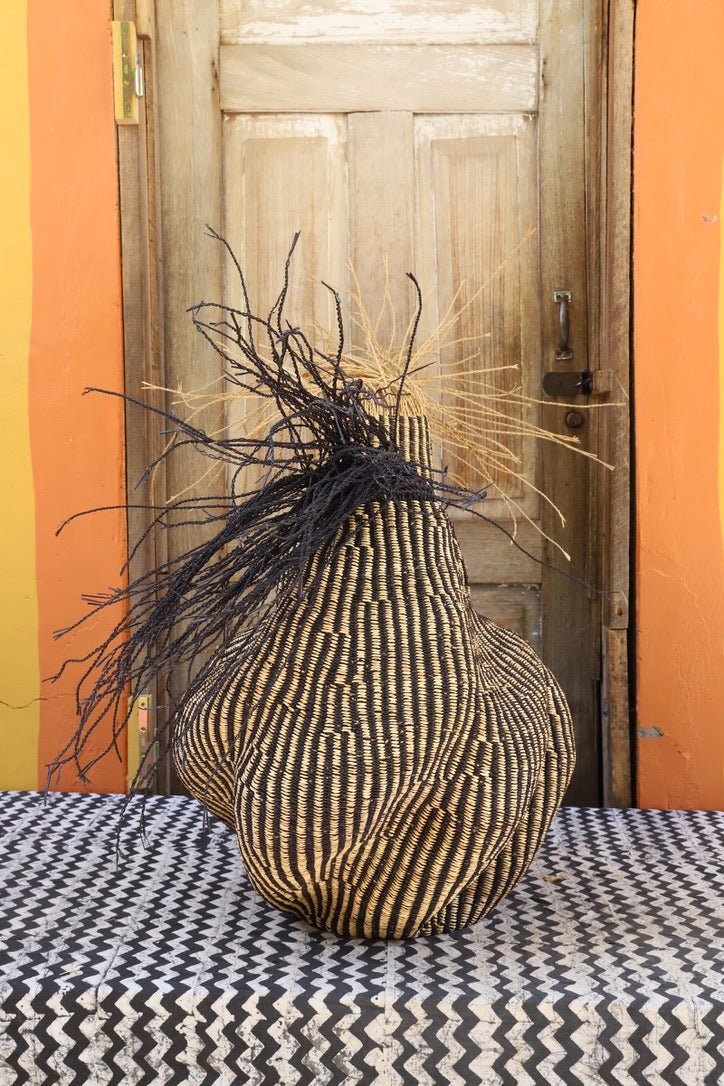 Decorative basket with stylish straw branching out on a black and white cloth against a wooden door.