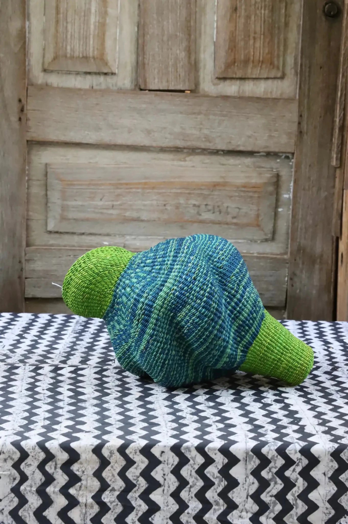 Woven conch piece on a black and white patterned surface with a wooden door in the background.