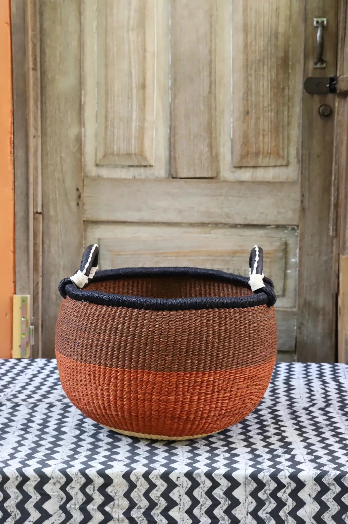 A colorful handwoven storage basket sitting on a black and white cloth against a wooden door
