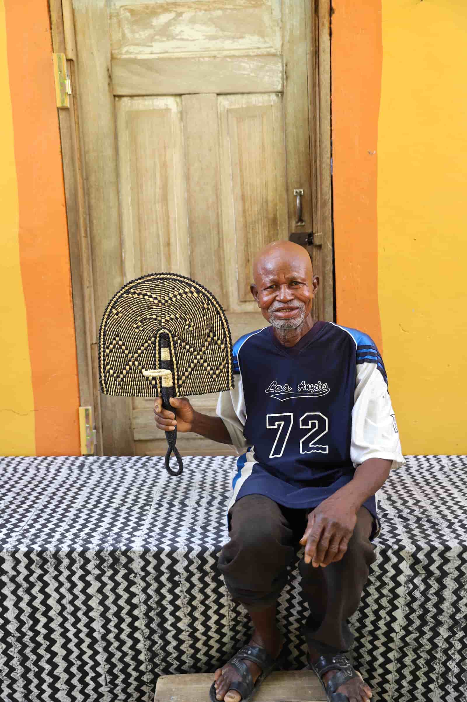 Man sitting on a bed holding a wooden object against a colorful wall.