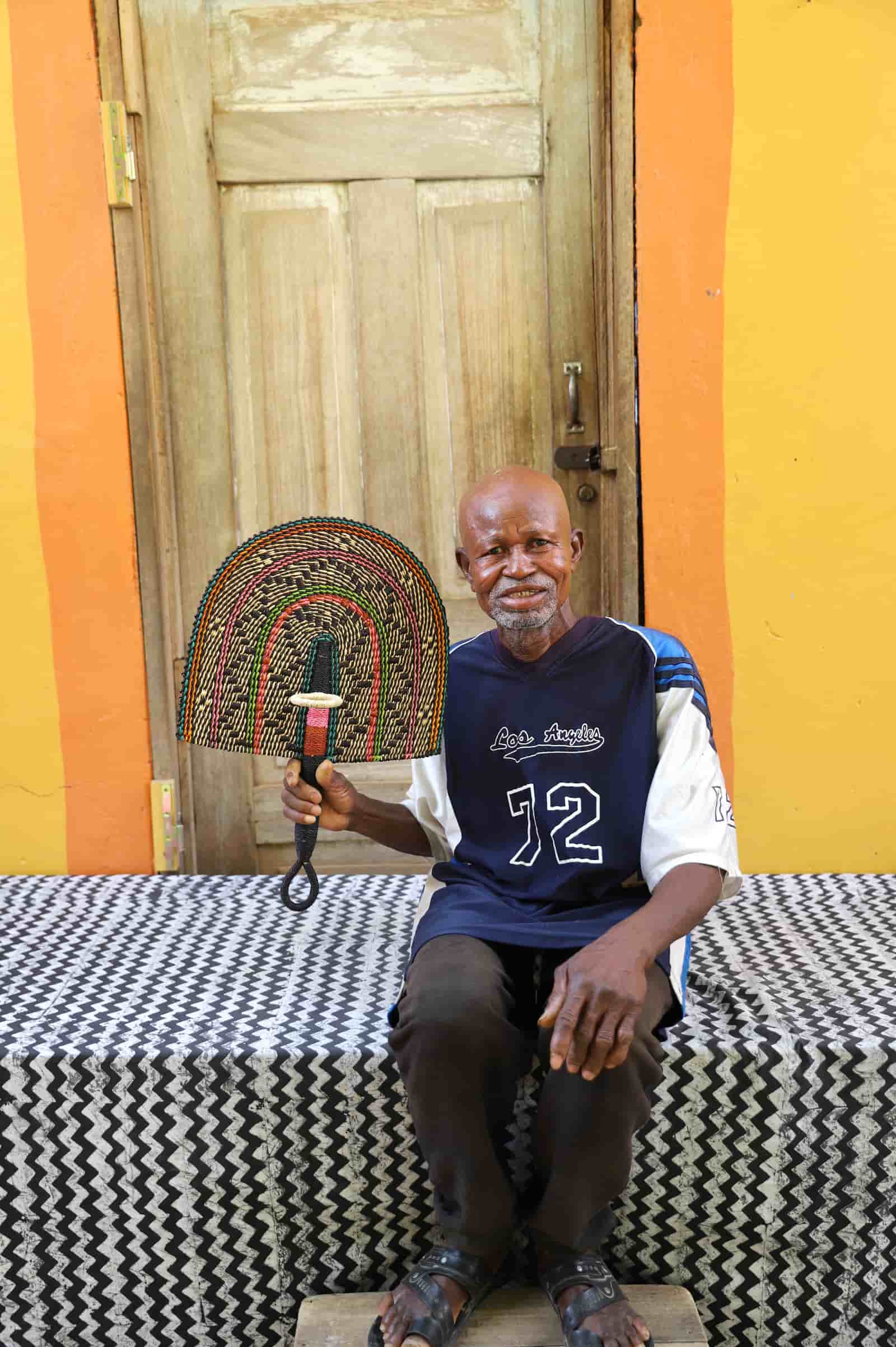Man holding a woven basket in front of a colorful wall with a wooden door.